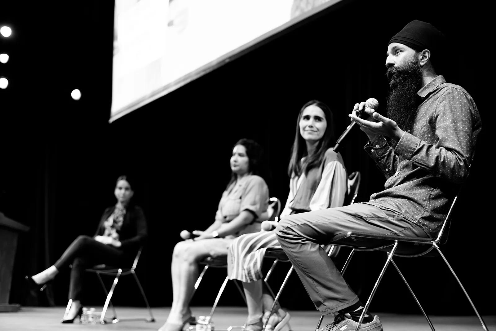 BW picture of panel of speakers with bearded, turbaned Sikh man speaking on mic, and three women